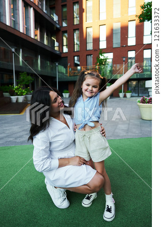 A mother and daughter enjoying a joyful moment outdoors in a modern urban setting during the summer 121633372