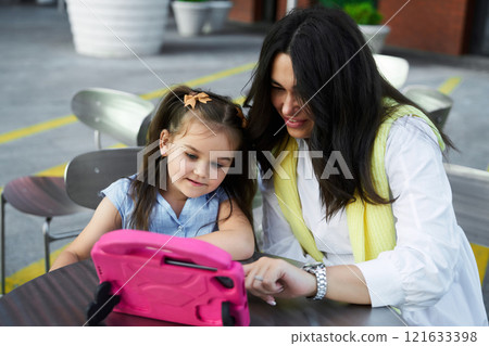 Mother and daughter enjoying time together while watching a video on a tablet outdoors Mother and daughter enjoying time together while watching a video on a tablet outdoors 121633398