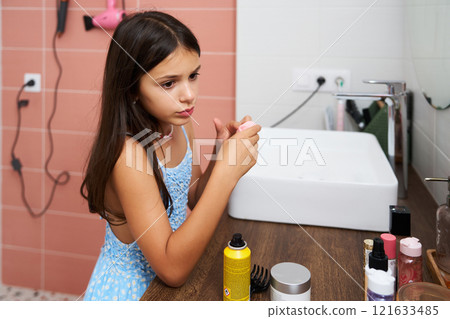 Young girl contemplating while sitting at a bathroom vanity with beauty products in the morning light 121633485