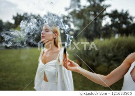Women in white attire engaging with smoke outdoors during daylight Women in white attire engaging with smoke outdoors during daylight 121633500