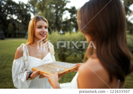 Two women in white dresses interact outdoors with a unique game set 121633507