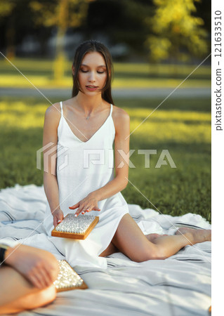Young woman relaxing on a blanket in a park while playing with a handheld game 121633510