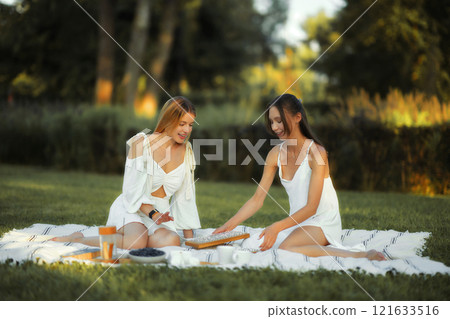 Friends enjoying a picnic in a serene park during a sunny afternoon Friends enjoying a picnic in a serene park during a sunny afternoon 121633516