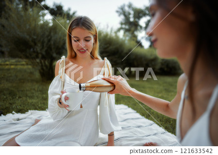 Friends enjoying a relaxing afternoon with tea in a sunny park setting 121633542