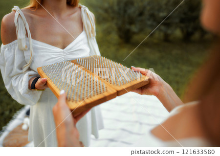 Person holding a wooden board with spikes during a wellness activity outdoors 121633580
