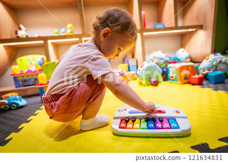 Young child exploring music with a toy piano in a vibrant play area 121634831