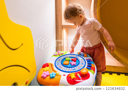 Young child engaged with educational activity table in bright and playful daycare environment Young child engaged with educational activity table in bright and playful daycare environment 121634832