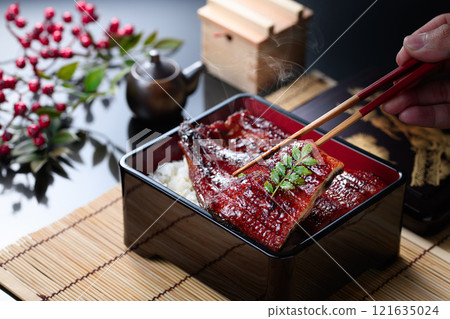 A sizzling Japanese food cut of steaming eel rice being picked up with chopsticks 121635024