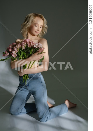 Woman kneeling with bouquet of flowers in a minimalist studio setting 121636005