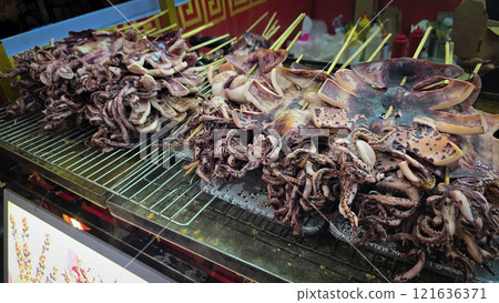 Freshly grilled barbecue squid on skewers displayed at an Asian street food market showcasing vibrant culinary traditions Freshly grilled barbecue squid on skewers displayed at an Asian street food market showcasing vibrant culinary traditions 121636371