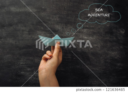 Hand holding a paper boat with the words Sea Adventure written above it Hand holding a paper boat with the words Sea Adventure written above it 121636485