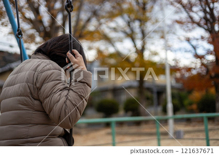 Back view of a middle-aged woman swinging alone in an empty park 121637671