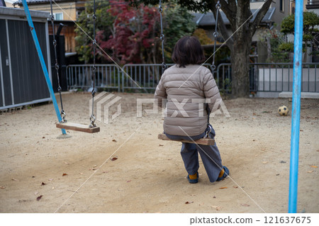 一名中年婦女在空蕩蕩的公園裡獨自盪鞦韆的後視圖 一名中年婦女在空蕩蕩的公園裡獨自盪鞦韆的後視圖 121637675