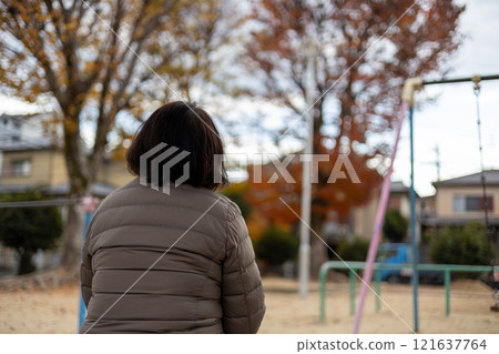 Back view of a middle-aged woman sitting in a park and daydreaming 121637764
