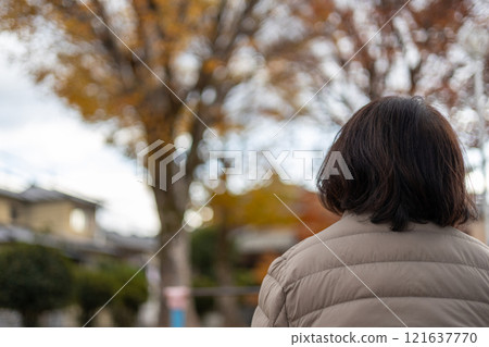 Back view of a middle-aged woman sitting in a park and daydreaming 121637770