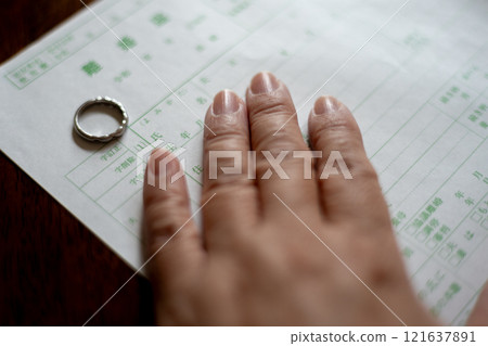 一位中年婦女的手，正在摘下結婚戒指，填寫離婚文件。 121637891