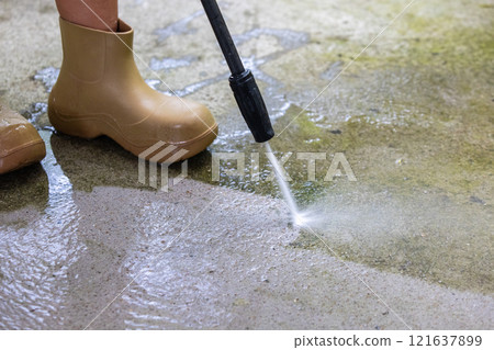 Woman cleaning concrete pavement using high pressure washer. 121637899