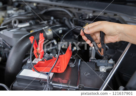 Senior Woman is jumping charger cable to AGM battery on car. 121637901
