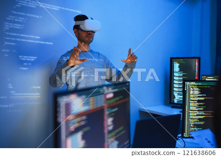 developer uses a VR headset to interact with projected interface designs, while colleagues discuss and code on screens, highlighting the integration of virtual reality and UI/UX design in modern 121638606