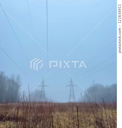 metal electrical towers stretch across a foggy landscape, with a dirt path . High quality photo 121638911