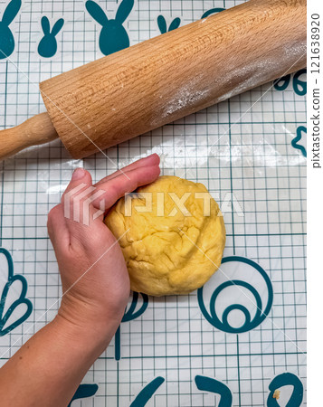 hand gently presses down on a ball of dough on baking mat, with a rolling pin . High quality photo 121638920