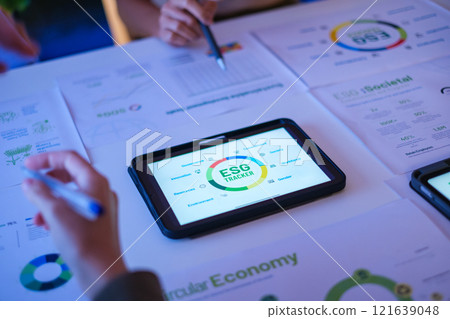 close up diversity team brainstorming focused on ESG (environment,social,governance)  with tablet or sdgs goals in a sustainable green office at night 121639048