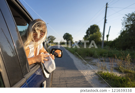 A beautiful woman driving a car enjoys the feeling of the wind in her hair and freedom. A woman looks out the open car window and the wind blows her hair. The concept of traveling by car. 121639338