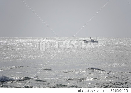 Sunlight breaks through the clouds, illuminating the calm sea and fishing boats. Sunlight breaks through the clouds, illuminating the calm sea and fishing boats. 121639423