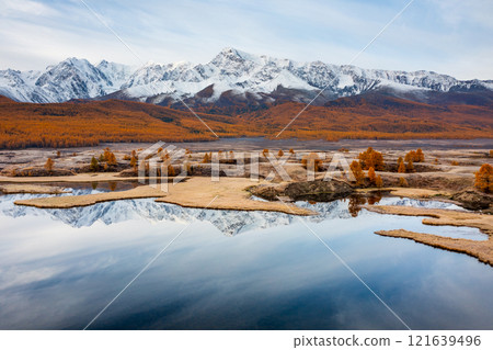 Snow-Capped Mountain Range with Orange Foliage Reflecting in Calm Lake 121639496