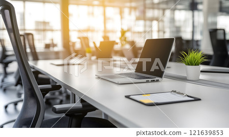 Laptop showing blank screen sitting on desk in modern open plan office 121639853