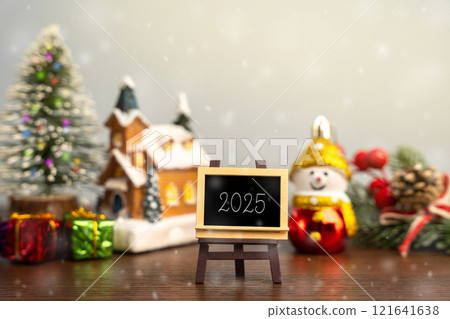 Easel with text Year 2025. Xmas winter holiday. Decoration, celebration. The concept of the beginning of the new year. Christmas tree, gifts and a house with snowfall 121641638