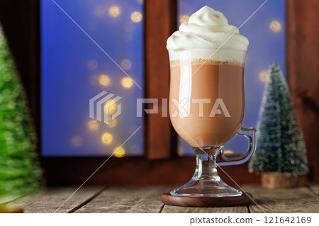 hot chocolate or cocoa with whipped cream in glass cup on table with window 121642169