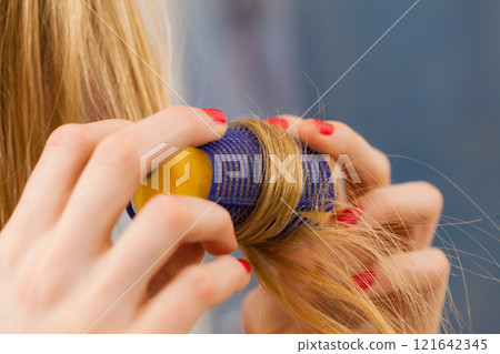 Woman curling her hair using rollers Woman curling her hair using rollers 121642345