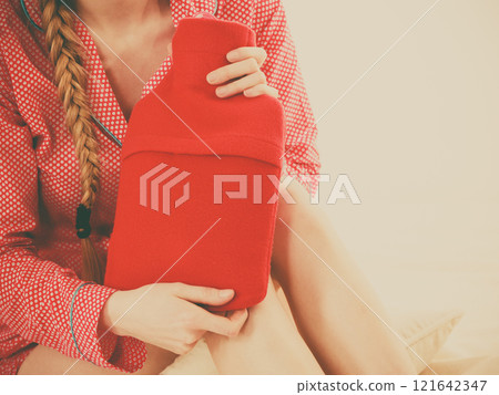 Woman holding warm red hot water bottle 121642347