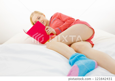 Woman relaxing in bed reading book 121642431