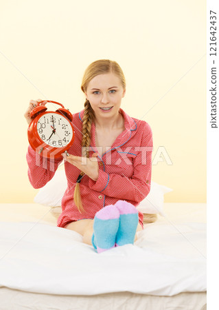 Sleepy woman wearing pajamas holding clock 121642437