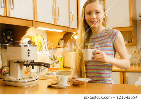 Woman in kitchen making coffee from machine 121642554
