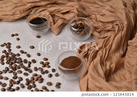 Fresh aromatic grain, ground and coffee drink in a small glasses, white background, brown cloth Fresh aromatic grain, ground and coffee drink in a small glasses, white background, brown cloth 121643814