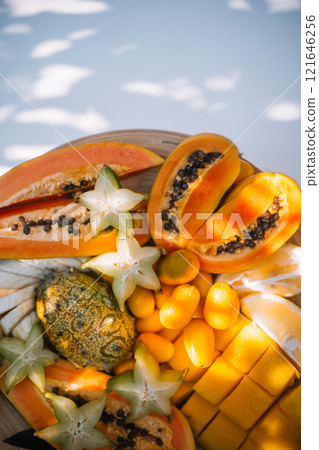 Fresh tropical fruits displayed on a wooden plate in natural light 121646256