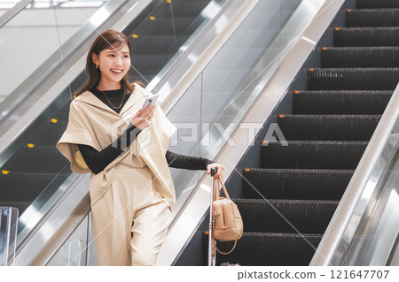 A young woman arrives at the airport and descends the escalator 121647707