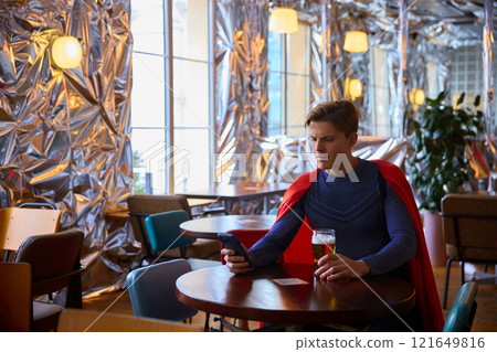 Man in cape holds phone, multitasking with beer, representing modern-day superheroes juggling technology, leisure, and responsibility in surreal setting. 121649816