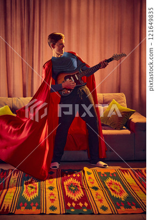 Standing tall with guitar in hand, man dressed as superhero strikes powerful pose, his cape flowing dramatically as he unleashes creativity. Standing tall with guitar in hand, man dressed as superhero strikes powerful pose, his cape flowing dramatically as he unleashes creativity. 121649835