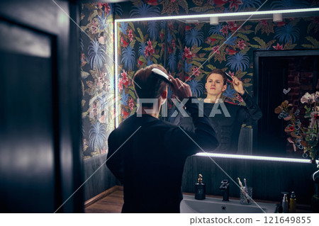 Man, dressed as superhero, combing hair in well-lit bathroom, calm precision highlighting balance of routine and care. 121649855