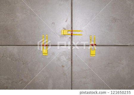 Close-up of tile leveling system with plastic clips and wedges in place. Perfect alignment during floor installation. Ideal for construction, renovation, and DIY projects Close-up of tile leveling system with plastic clips and wedges in place. Perfect alignment during floor installation. Ideal for construction, renovation, and DIY projects 121650235
