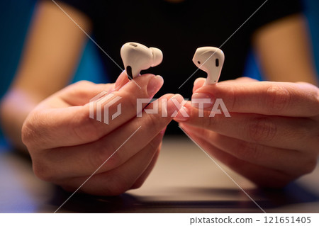 Closeup image of a person holding a pair of wireless earbuds firmly in their hands Closeup image of a person holding a pair of wireless earbuds firmly in their hands 121651405
