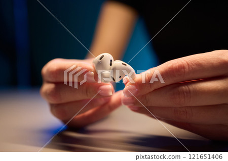 Closeup image of a person holding a pair of wireless earbuds firmly in their hands 121651406
