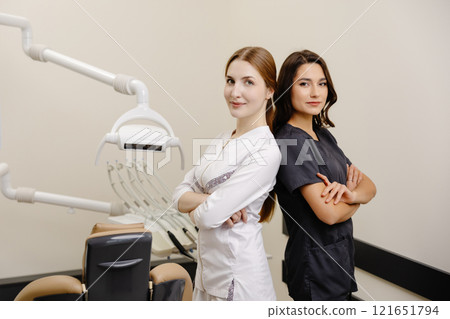 Smiling dentist and assistant with crossed hands looking at the camera in dental clinic Smiling dentist and assistant with crossed hands looking at the camera in dental clinic 121651794