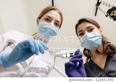 From below female dentists with mirror and device bending over patient during appointment in dental clinic From below female dentists with mirror and device bending over patient during appointment in dental clinic 121651795