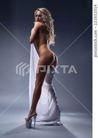 Athletic naked woman wearing white fabric in studio and looking into camera Athletic naked woman wearing white fabric in studio and looking into camera 121652014