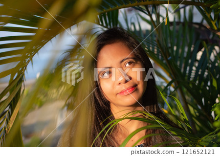 portrait of a beautiful young Filipina woman against a background of palm leaves in the rays of the sun portrait of a beautiful young Filipina woman against a background of palm leaves in the rays of the sun 121652121